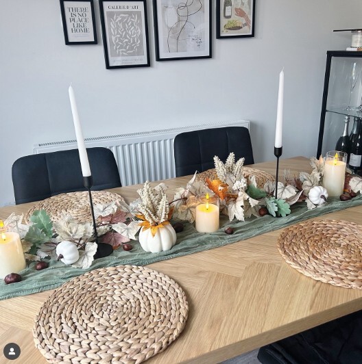 wood dining table with woodland autumnal tablescape featuring pumpkins, leaves and tall candles