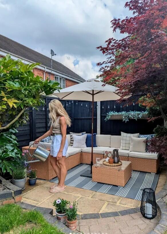 beige rattan modular 6 seat garden sofa with cream cushions in modern garden with parasol and young woman with blonde hair