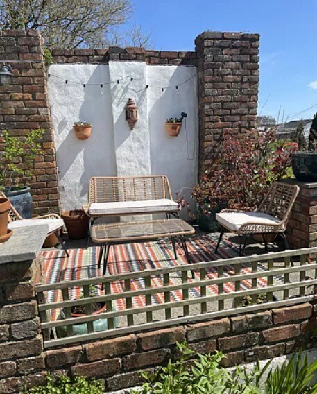Beige Rattan 4 Seat Garden Sofa & Chairs Set on striped rug in urban paved garden with brick wall and wall planbters behind