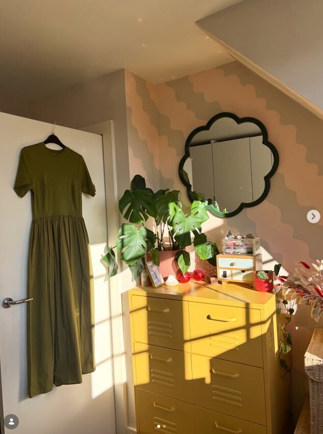 bold colourful room with srtiped salmon and grey walls, yellow metal storage chest of drawers and black wiggle frame mirror