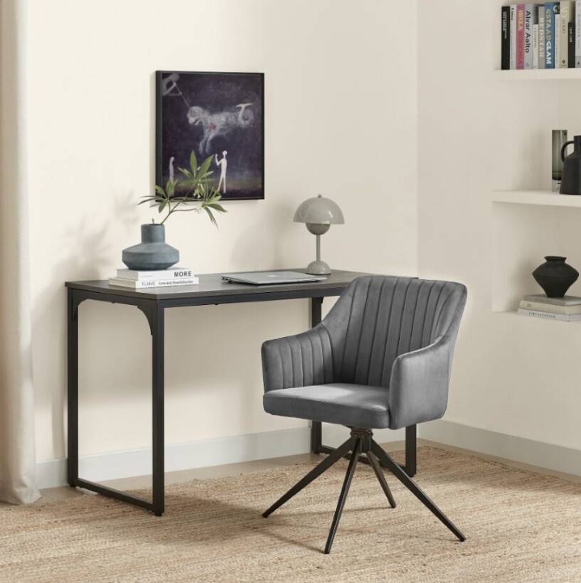 grey vevlet swivel chair with black legs in front of wooden desk