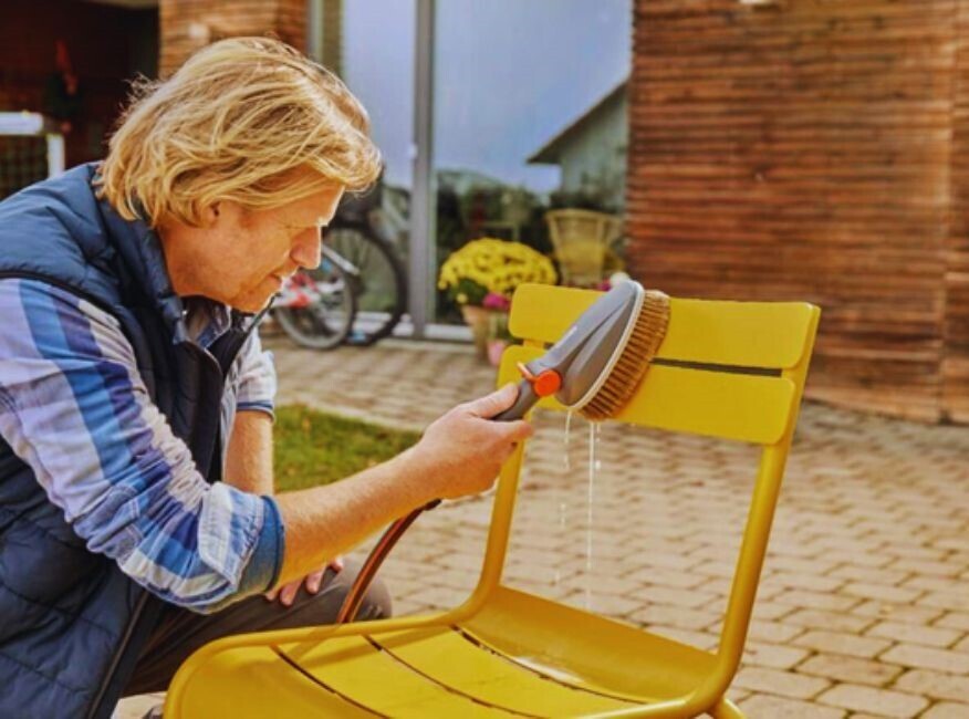 man cleaning yellow metal garden chair with soft brush