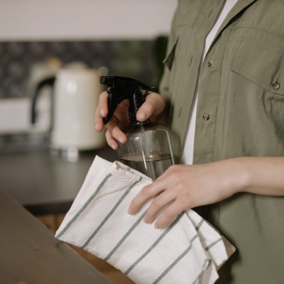 person holding a spray bottle and cleaning cloth, wearing gloves