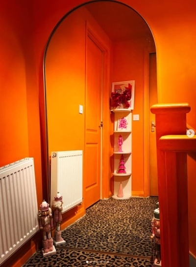 bold orange hallway with orange painted stair banister and gold metal arch floor mirror