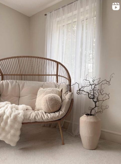 rattan double egg chair in a cosy bedroom nursery, with cream cushions and throw, beside decorative plant pot, beside window