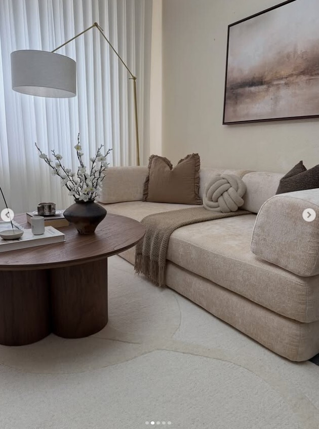 modern warm cosy living room with cream sofa dressed in complimentary neutral cushions and throw