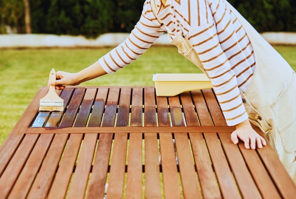 person painting a wooden garden table with wood treatment
