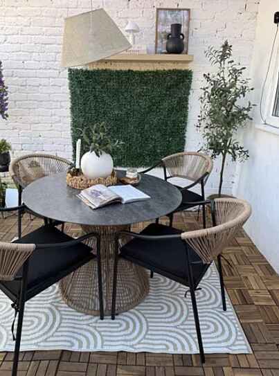 round black metadl garden dining table with matching chairs in covered outdoor living area with overhead lampshade, shelf in background, and planting