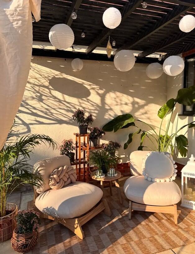 2 wooden garden accent chairs with plump cream cushions in boho-styled pergoda space with plants and lanterns