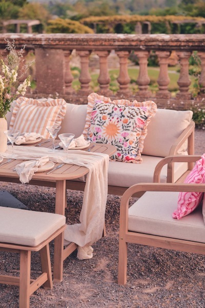 garden dining table and chairs styled with colouful outdoor cushions and tableware in front of stone wall