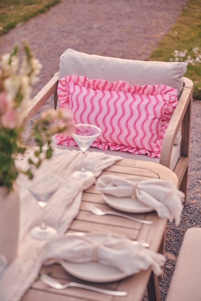 close up detail of garden dinig table, with pretty place settings and martinin glasses, wooden garden dining chair with pink striped cushion