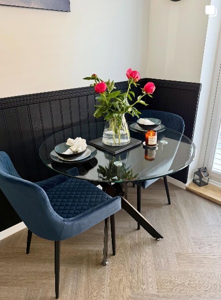 modern round glass and black metal dining table with 2 navy blue velvet chairs in black paneled dining area
