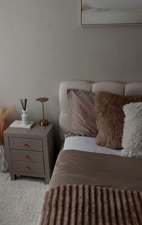 modern glam bedroom with bed styling in glam warm neutrals, with layered textured cushions and mirrored taupe glass bedside table