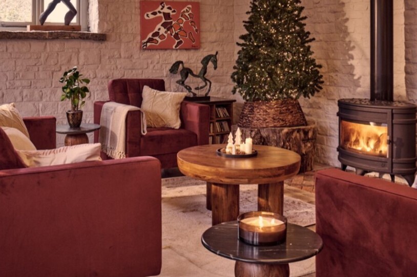 warm living room with maroon velvet sofas, cream rug, wood coffee table, fireplace and Christmas tree