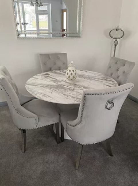round marble pedestal dining table with 4 grey velvet knockerback dining chairs in front of sivler framed wall mirror
