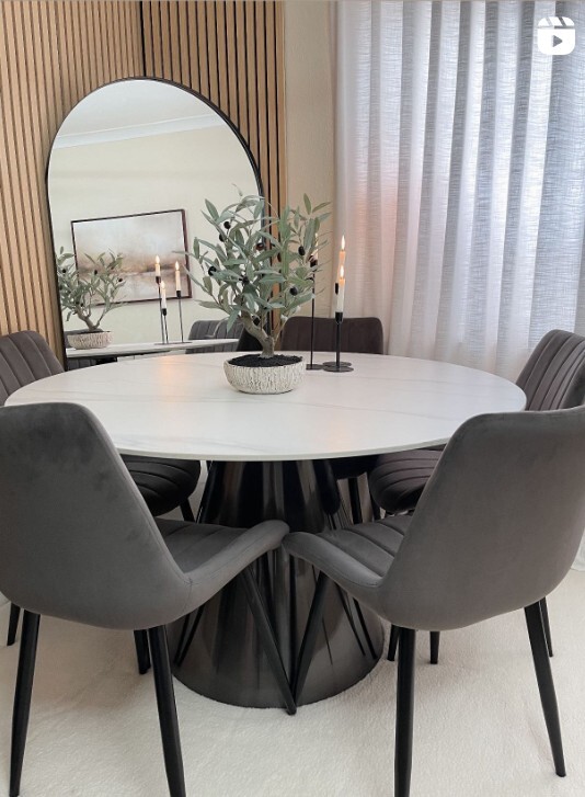modern round pedestal dining table with fabric chairs and large wall mirror behind