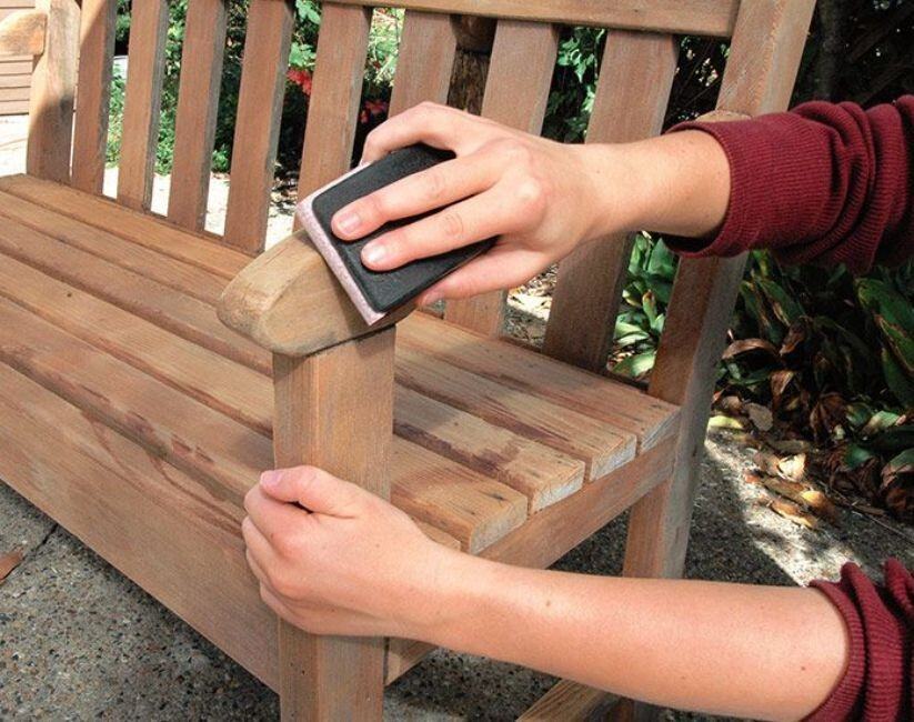 person sanding arm of wooden garden bench