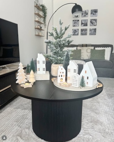 black wooden round coffee table with Scandi Christmas Decor styling of small Christmas village and fire trees