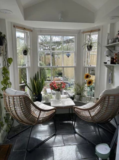 2 rattan chairs indoors at small dining table in bay window overlooking garden