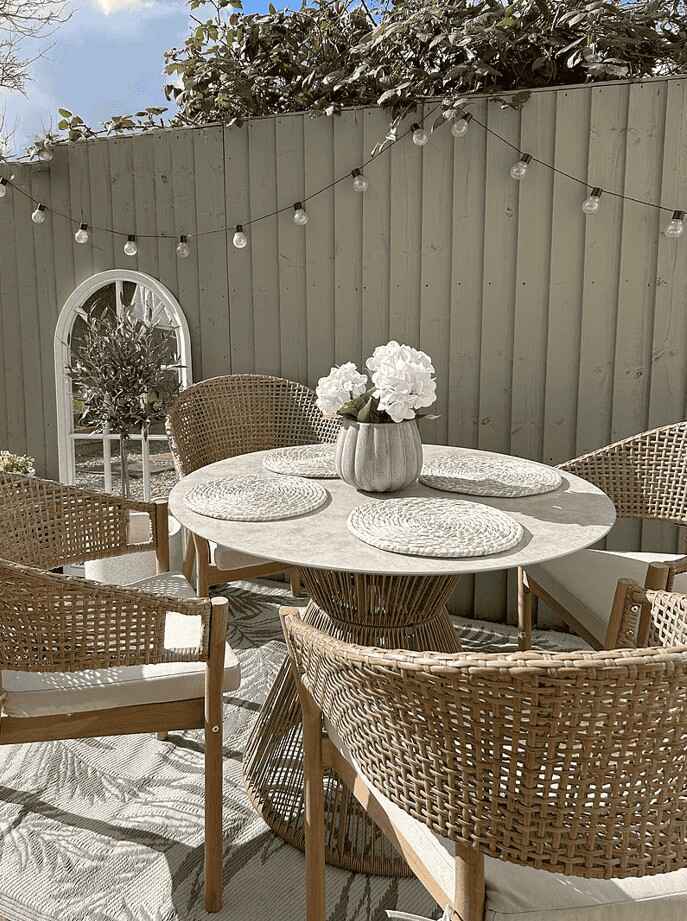garden makeover ideas featuring round rattan garden table and chairs, fairy lights and outdoor mirror