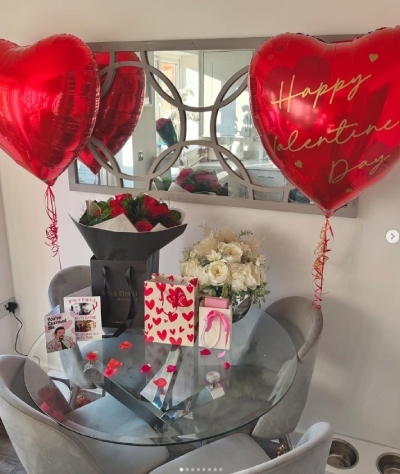 round glass dining table, grey chairs, set for Valentines dinner table at home with red balloons, gifts and flowers