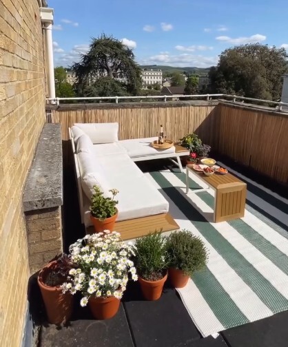 white metal corer garden sofa with cream cushions on balcony with striped rug and flower pots