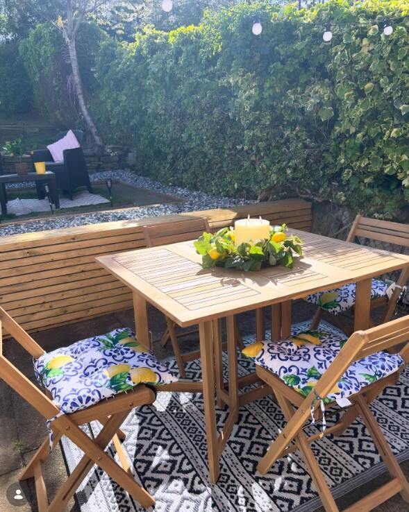 Wood 4 Seat Folding Table Garden Dining Set on rug beside wooden planters and beside hedge with fiary lights